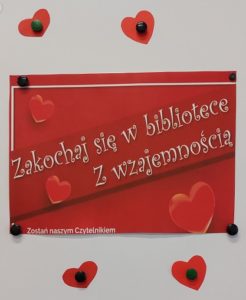 Zdjęcie przedstawia plakat "Zakochaj sie w bibliotece". Napis białymi literami na czerwonym tle i kilka serduszek.